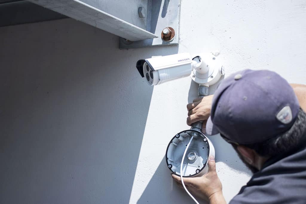 Technician mounting a weather-rated bullet security camera with a junction box on a commercial wall in Miami